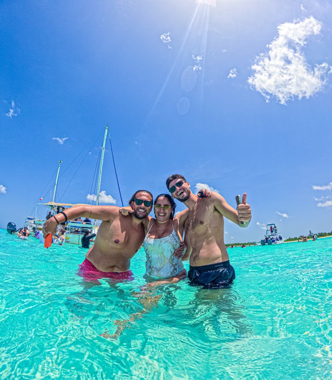 Tres amigos posando en aguas turquesa con veleros al fondo