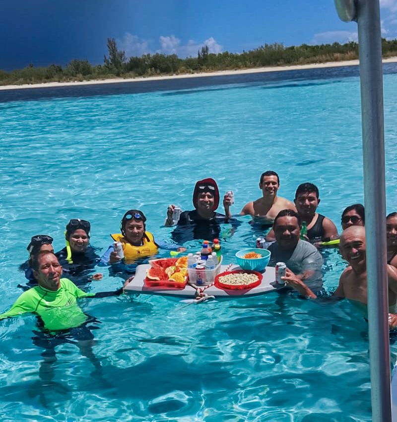 Grupo de amigos compartiendo botanas en una mesa flotante dentro del mar