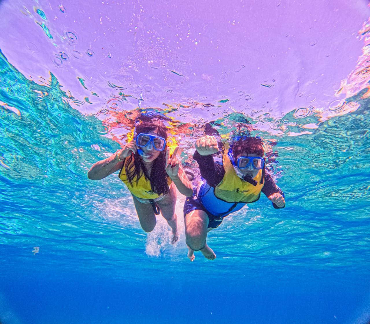Dos amigas nadando hacia la cámara con chalecos y snorkel